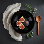 High-glaze black stoneware bowl lifestyle shot styled with figs, wooden spoon and eucalyptus